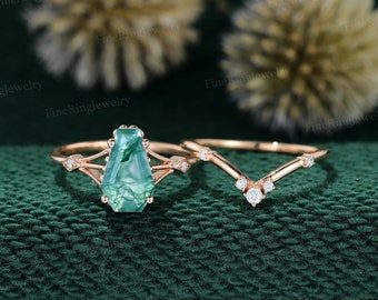 May include: A rose gold engagement ring set with a green agate gemstone and a matching rose gold band with small diamonds. The ring is on a green fabric background.