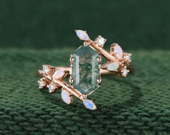 May include: A rose gold ring featuring a central hexagonal moss agate stone. The band is designed with branch-like metalwork adorned with small, marquise-cut opals and round, clear accent stones extending from the center setting.