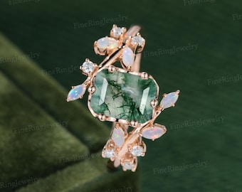 May include: A rose gold ring featuring a rectangular moss agate center stone with green inclusions, surrounded by small marquise-cut opals and round white accent stones arranged in a branch-like setting along the band.