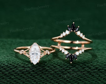May include: A rose gold engagement ring set with a pear-shaped center stone and a matching rose gold wedding band with black and white diamonds.