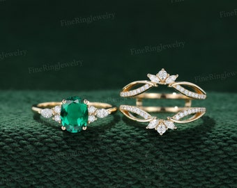 May include: A gold ring set with a large emerald green gemstone surrounded by smaller diamonds. A matching gold ring with diamonds is designed to fit around the engagement ring.