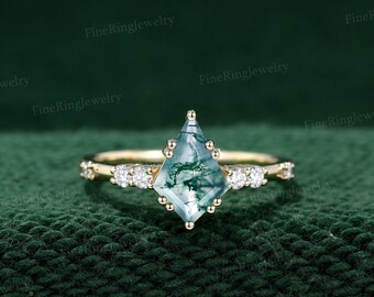 May include: A gold ring with a green moss agate gemstone in a kite shape. The ring is set with small diamonds on the band.