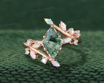May include: A rose gold ring featuring a kite-shaped moss agate center stone. The band is designed with a branch-like motif, accented with small, marquise-cut opals and round white stones arranged along the sides of the central setting.