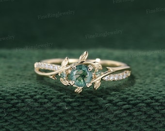 May include: A gold ring with a green gemstone surrounded by smaller diamonds. The ring features a delicate design with leaves and branches.