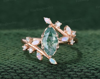 May include: A rose gold ring featuring a central marquise-cut moss agate stone, accented with small round white diamonds and marquise-shaped opals arranged in a branch-like design along the band, creating a botanical-inspired appearance.