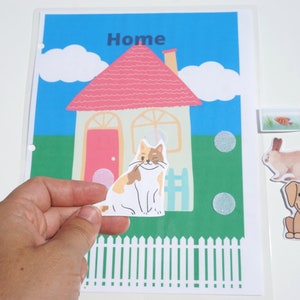 May include: A colourful felt board with a house, a cat, a rabbit and a dog. The house has a pink roof and a red door. The cat is white with orange and brown markings. The rabbit is brown and white. The dog is brown and white with a yellow collar. The board has the word "Home" written on it.