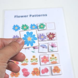 Può includere: Un fiore blu con un centro giallo su una carta bianca. La carta fa parte di un gioco di abbinamento di motivi floreali.