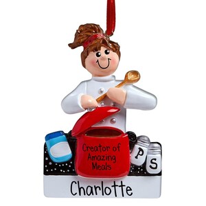 May include: A Christmas ornament featuring a chef with brown hair and a red headband, stirring a pot. The pot is red and says "Creator of Amazing Meals." Includes salt and pepper shakers and the name "Charlotte."
