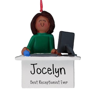 Puede incluir: Un adorno navideño personalizado que representa a una mujer de dibujos animados con cabello castaño y un suéter verde sentada en un escritorio con una computadora. El adorno tiene el nombre "Jocelyn" y el texto "Mejor recepcionista de todos los tiempos".