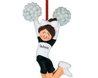 May include: A cheerleader ornament in a jumping pose, holding white pom-poms. The ornament features a black and white uniform with the name "DeAnna" printed on the front. The ornament is suspended by a red ribbon.