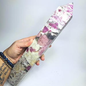 May include: A tall, faceted crystal tower featuring a mix of opaque white, grey, and translucent sections with prominent inclusions of vibrant magenta and deep pink mineral deposits throughout the stone's elongated, pointed structure.
