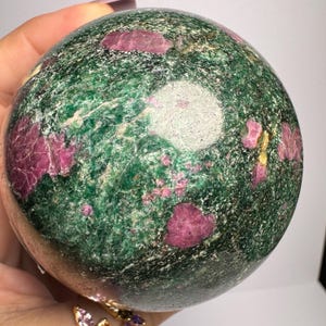 May include: A green and pink sphere with a smooth, polished surface. The sphere is made of a natural stone with a variety of colours and textures.