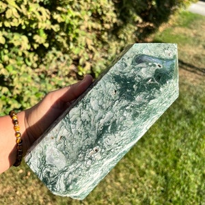 May include: A green and white marbled crystal point, also known as a green moss agate, is a natural stone with a unique pattern. The crystal point is a polished, faceted, and pointed shape.