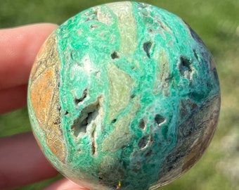 Puede incluir: Una esfera verde, marrón y blanca con un patrón de remolino. La esfera está hecha de piedra natural y tiene una superficie lisa y pulida.