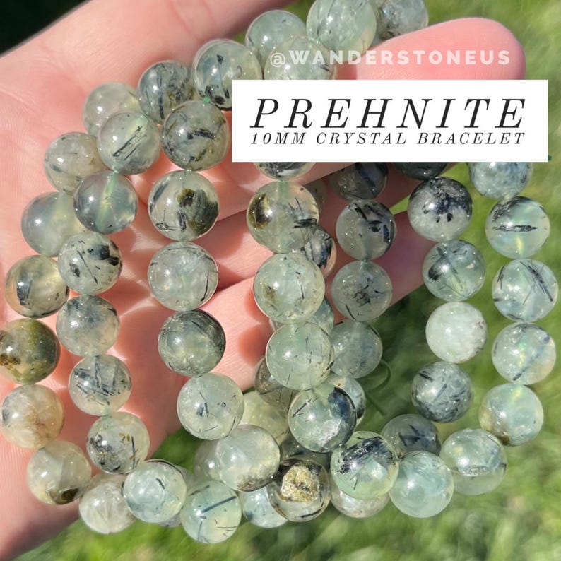 May include: A green prehnite crystal bracelet with black inclusions. The bracelet is made with 10mm round beads and is shown on a person's wrist. The text "PREHNITE 10MM CRYSTAL BRACELET" is visible in the image.