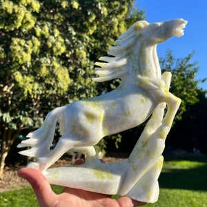 May include: A white jade horse sculpture with green accents. The horse is rearing up on its hind legs and has a flowing mane. The sculpture is carved in a realistic style and is a beautiful example of jade carving.