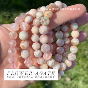 Puede incluir: Un brazalete hecho con cuentas de ágata de flor de 8 mm. Las cuentas son una mezcla de rosa, blanco y marrón con un patrón de remolino. El brazalete está hecho con hilo elástico.