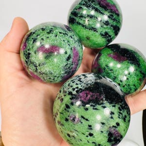 Könnte beinhalten: Vier grüne, schwarze und rosafarbene Edelsteinkugeln. Die Kugeln sind poliert und haben eine glatte, glänzende Oberfläche.