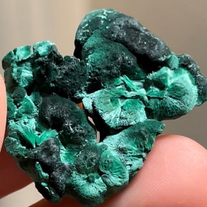 Op de afbeelding: Een groen malachiet mineraal specimen met een ruw, getextureerd oppervlak. De malachiet heeft een diepgroene kleur met enkele zwarte accenten.