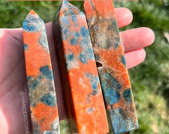 May include: Three polished crystal points, one blue apatite and two sunstone, with a mix of orange and blue colors. The crystals are held in a hand. @wanderstone.us