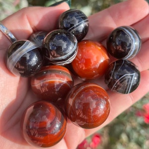 May include: A collection of agate spheres in various shades of brown, red, and black. The spheres are polished and have a smooth, shiny surface.