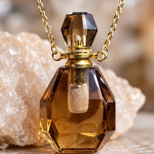 May include: A faceted, translucent brown glass perfume bottle pendant suspended from a gold-toned metal chain. The bottle features a geometric, multi-sided shape with a matching brown glass stopper and a gold-colored metal collar at the neck.
