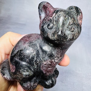 May include: A carved stone cat figurine in shades of black and burgundy. The cat is in a seated position with its ears perked up and eyes open. The stone has a polished, textured appearance.