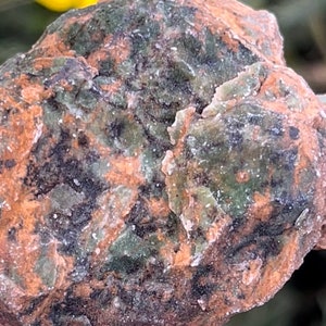 May include: A close-up of a green, brown, and white speckled rock. The rock has a rough, uneven surface.