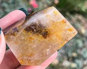 May include: A clear quartz crystal with a golden brown inclusion. The crystal is faceted and has a pyramid shape.