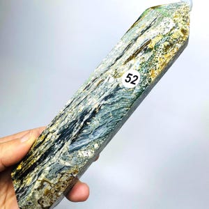 May include: A polished, elongated crystal tower featuring a complex, marbled pattern of deep blue, charcoal black, white, and golden-brown mineral inclusions. A small, circular white sticker with the black number 52 is affixed to the center.