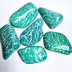 May include: A collection of six Amazonite stones in various shapes. The stones are a vibrant teal color with white veining patterns. The polished stones are smooth and appear to be natural gemstones, perfect for crystal enthusiasts.