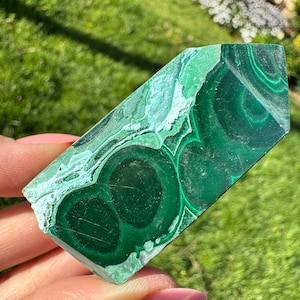 May include: A green malachite crystal point with a unique swirling pattern. The crystal is polished and has a smooth, glossy finish.