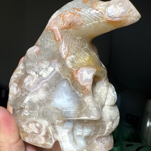May include: A carved stone sculpture of a reptile-like creature with a skull-like base. The sculpture is primarily clear with white, orange, and brown inclusions. The reptile head is angled upward.