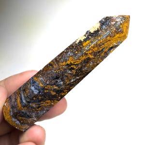 May include: A polished stone tower with a hexagonal point, featuring a swirling pattern of deep blue, dark brown, and vibrant mustard yellow colors. The mineral surface displays intricate, marbled textures throughout the elongated crystal form.
