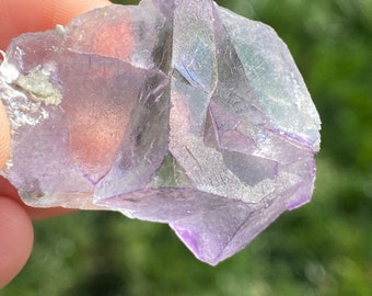 May include: A purple fluorite crystal with a geometric shape and a translucent appearance. The crystal has a natural, rough texture and is a beautiful example of this mineral.