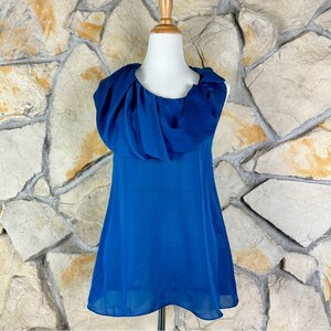 Pode incluir: Um vestido azul sem mangas com um grande decote de gola.