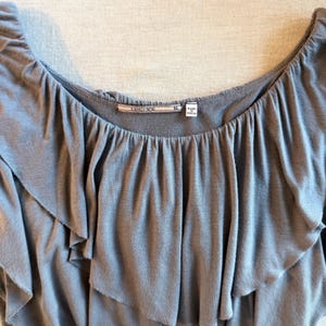May include: A gray off-the-shoulder top with layered ruffles. The top has a scoop neckline and the brand name "LANGUAGE" is visible on a tag. The size is XL and the tag says "Made in China".