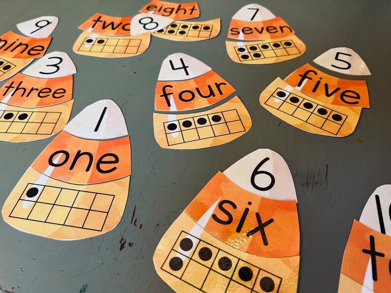 May include: A set of ten candy corn shaped cards with numbers 1 through 10, the word for each number, and a ten-frame with dots to represent the number. The cards are orange, yellow, and white.
