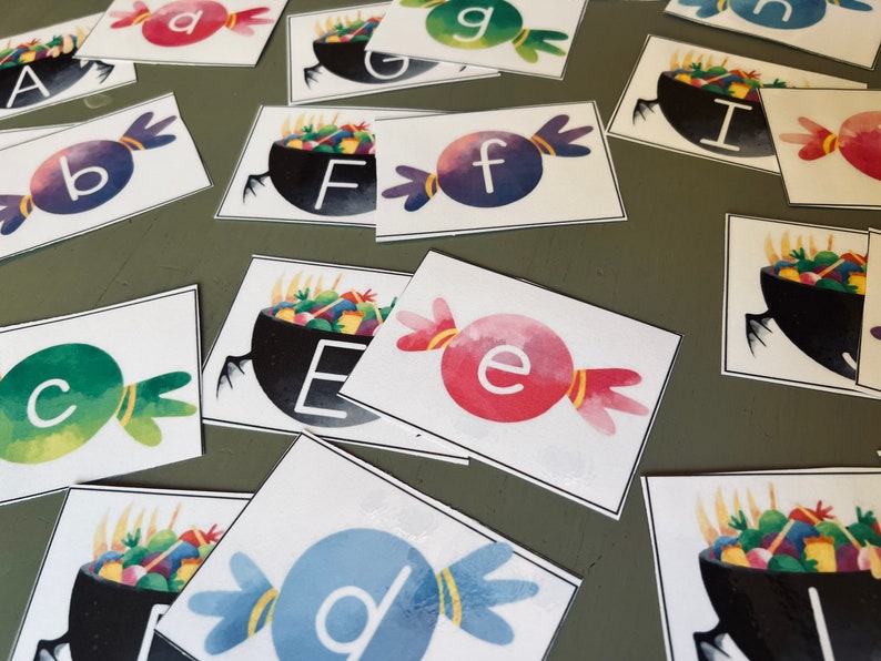 May include: A set of alphabet letter cards featuring a candy and a cauldron with colorful candy inside. The letters are a, b, c, d, e, f, g, i.