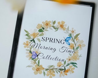 May include: A framed print with a watercolour floral wreath of yellow flowers and green leaves. The words "SPRING Morning Time Collection" are inside the wreath, with two blue butterflies. The frame is black.