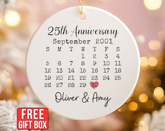 May include: A round white ceramic ornament featuring the text 25th Anniversary and September 2001 above a calendar grid. The number 30 is highlighted with a small pink heart. The names Oliver & Amy are printed in black script at the bottom.