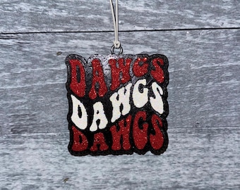 Pode incluir: Ornamento de glitter vermelho, branco e preto com a palavra "DAWGS" escrita três vezes em uma fonte retrô.