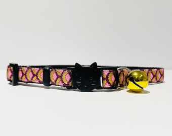 May include: A pink and gold patterned cat collar with a black cat head buckle and a gold bell.