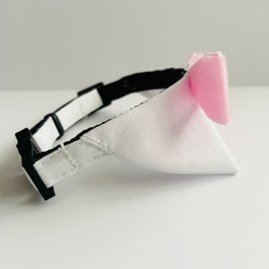 May include: A white and pink dog collar with a black adjustable buckle. The collar has a white fabric bow with a pink fabric accent.