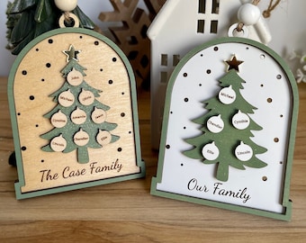 Op de afbeelding: Twee houten kerstboomversieringen met groene bomen en gouden sterren. De versieringen hebben een witte achtergrond met bruine stippen en de tekst "The Case Family" en "Our Family".
