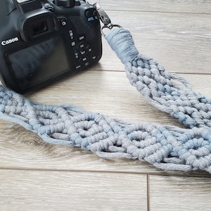 May include: A gray and blue macrame camera strap with a Canon DSLR camera attached.