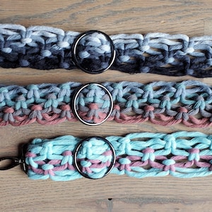 May include: Three crocheted macrame cord belts with black metal rings. The belts are in shades of blue, pink, and gray.
