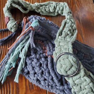 May include: A gray crocheted bag with a green crocheted strap and brown leather accents. The bag has a zipper closure and a metal ring.