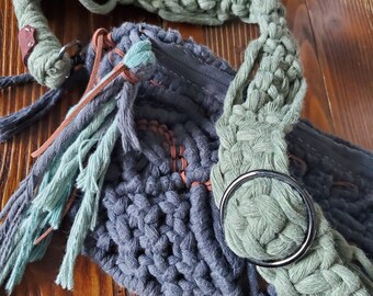 May include: A gray crocheted bag with a green crocheted strap and brown leather accents. The bag has a zipper closure and a metal ring.