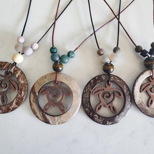 May include: Four necklaces with coconut shell pendants featuring a carved turtle design. Each necklace has a different colored set of beads: beige, green, brown, and black.
